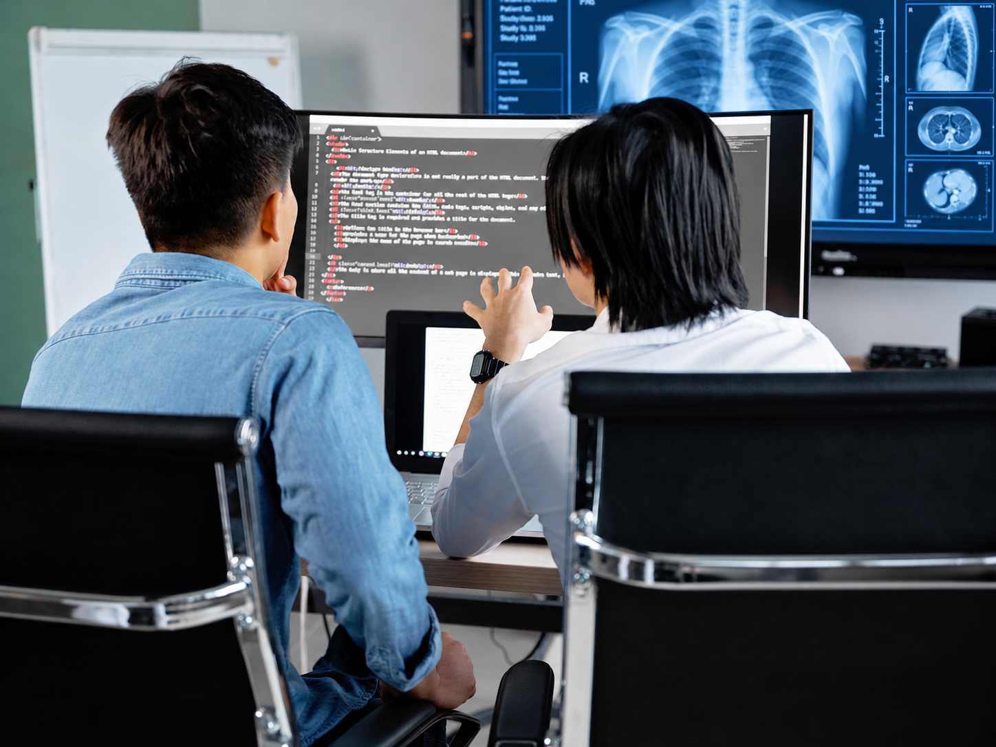 Two engineers reviewing code on a screen beside a medical imaging display